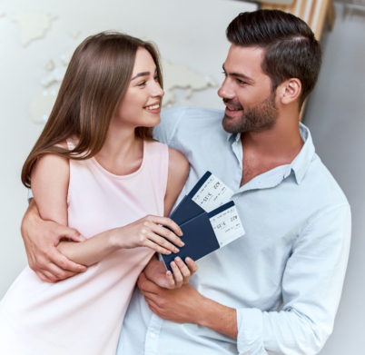 Portrait of joyful glad couple holding passport with flying tickets in hands pointing with forefinger looking to each other on map background